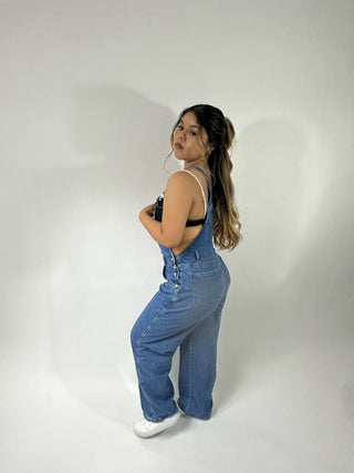 A girl wearing dark denim overalls with a white backdrop behind her 